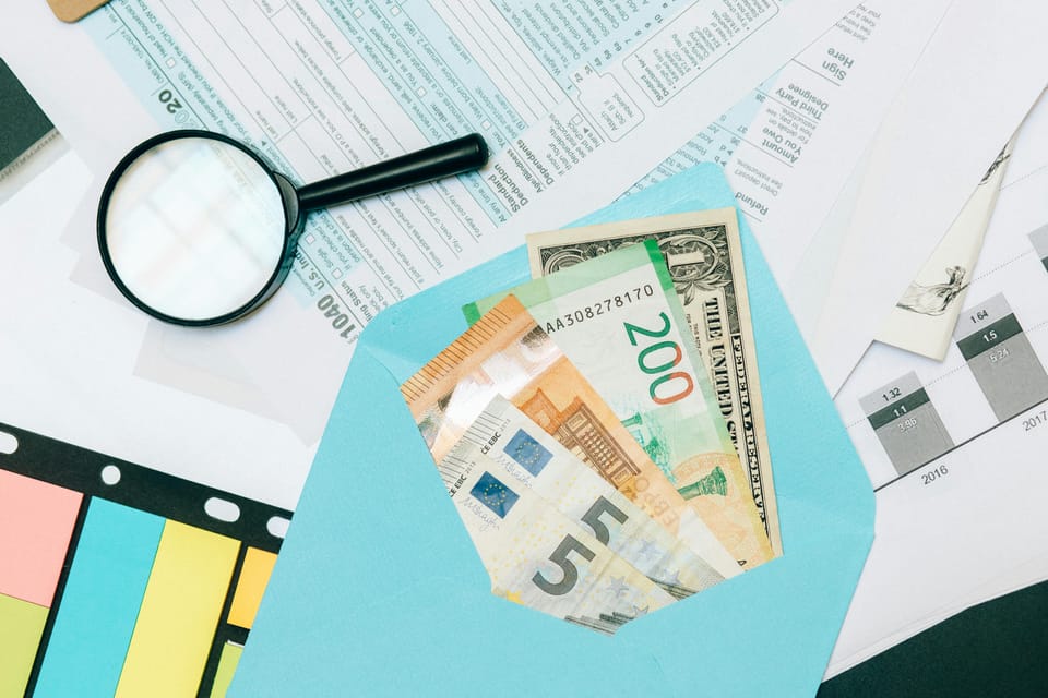 A magnifying glass and an envelope filled with cash resting on top of some tax paperwork